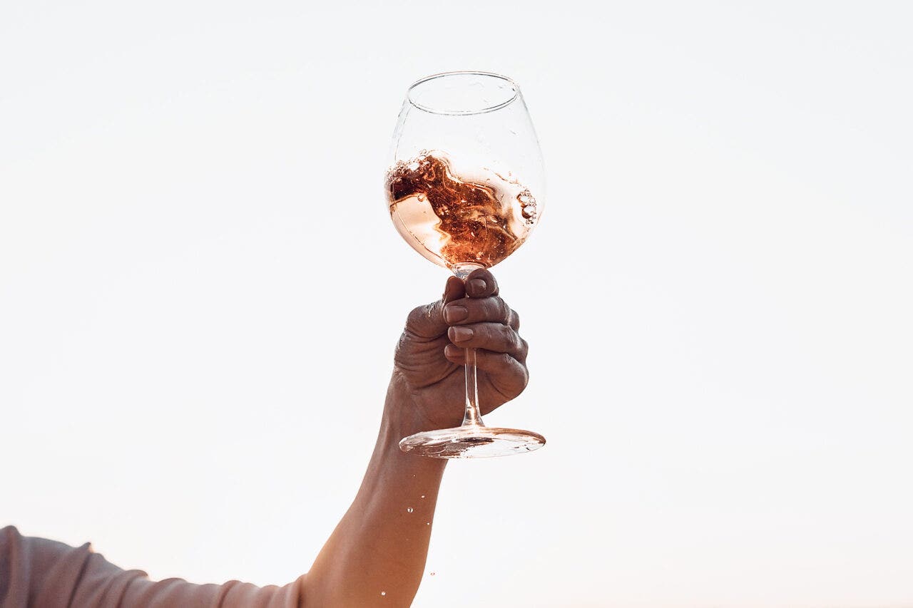Glass of Rosé with splashes in woman's hand against the sunset sky. Cropped.